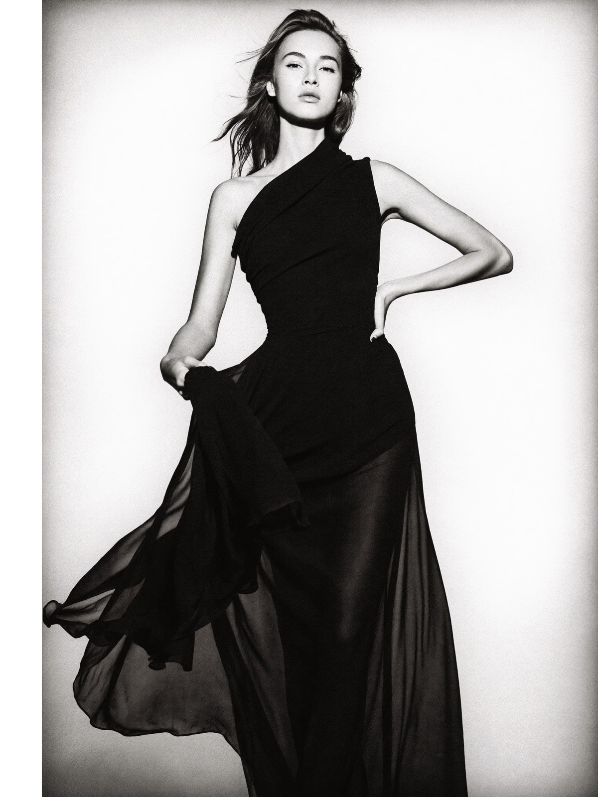 Full-length portrait of a woman in a flowing black gown against the signature white backdrop