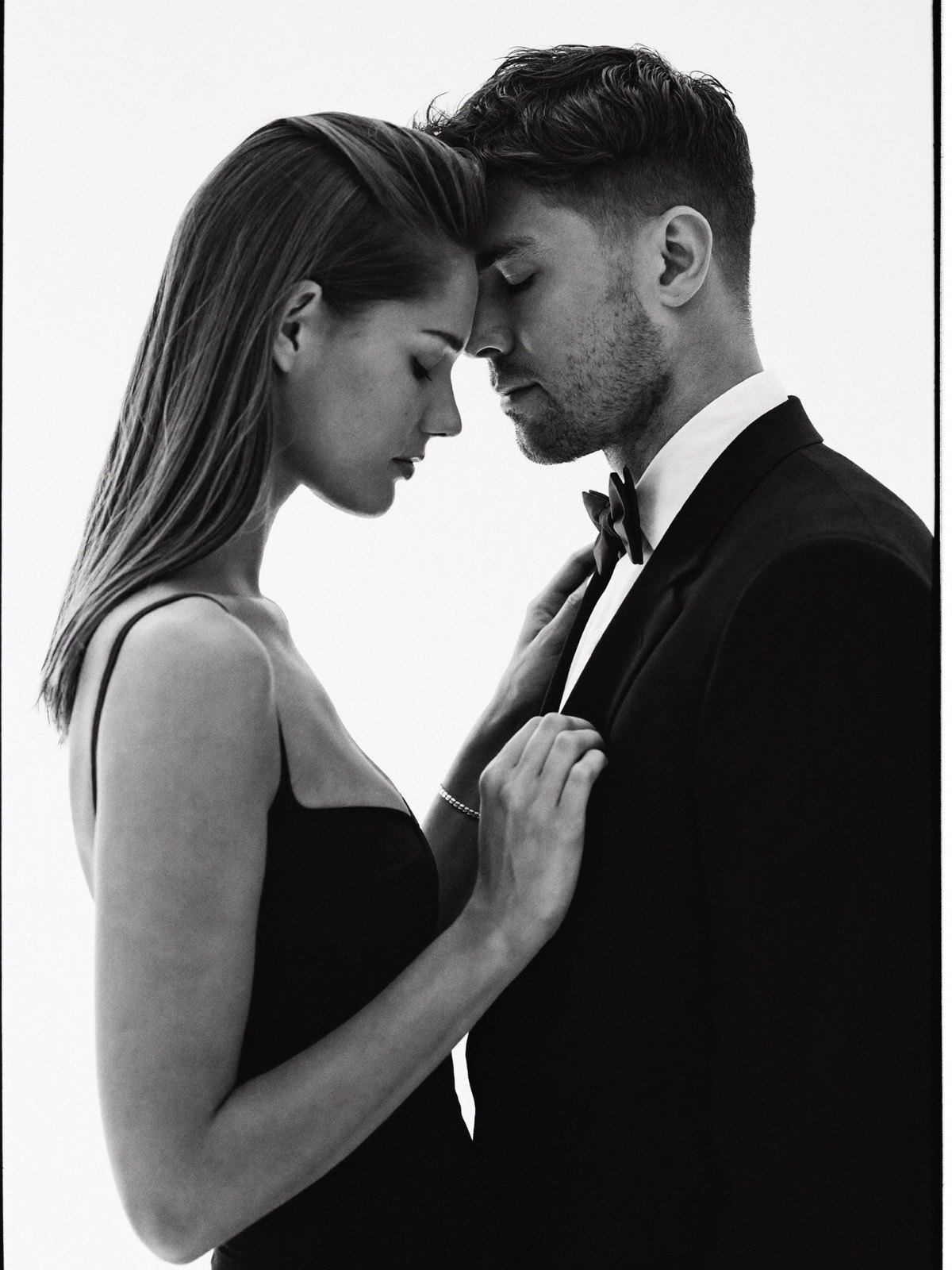 A couple in evening attire standing forehead to forehead, eyes closed