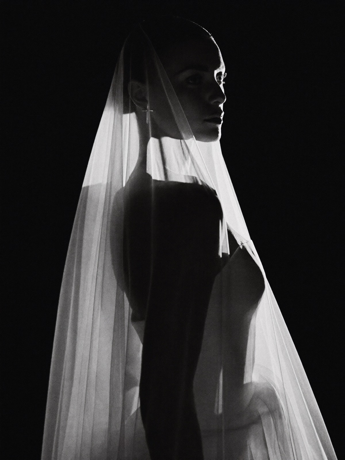 Bride in profile, her long veil glowing in backlight against a black backdrop